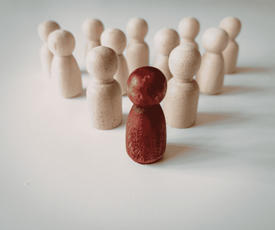 A red wooden peg figure standing ahead of a group of natural wooden figures, representing being proactive and getting ahead of yourself in productivity.