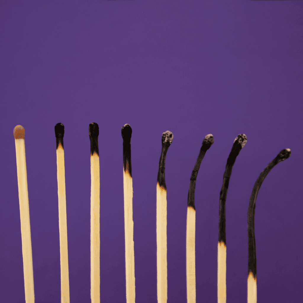A row of matches burning progressively from left to right, ending in completely charred and bent sticks, symbolizing burnout from hustle culture.