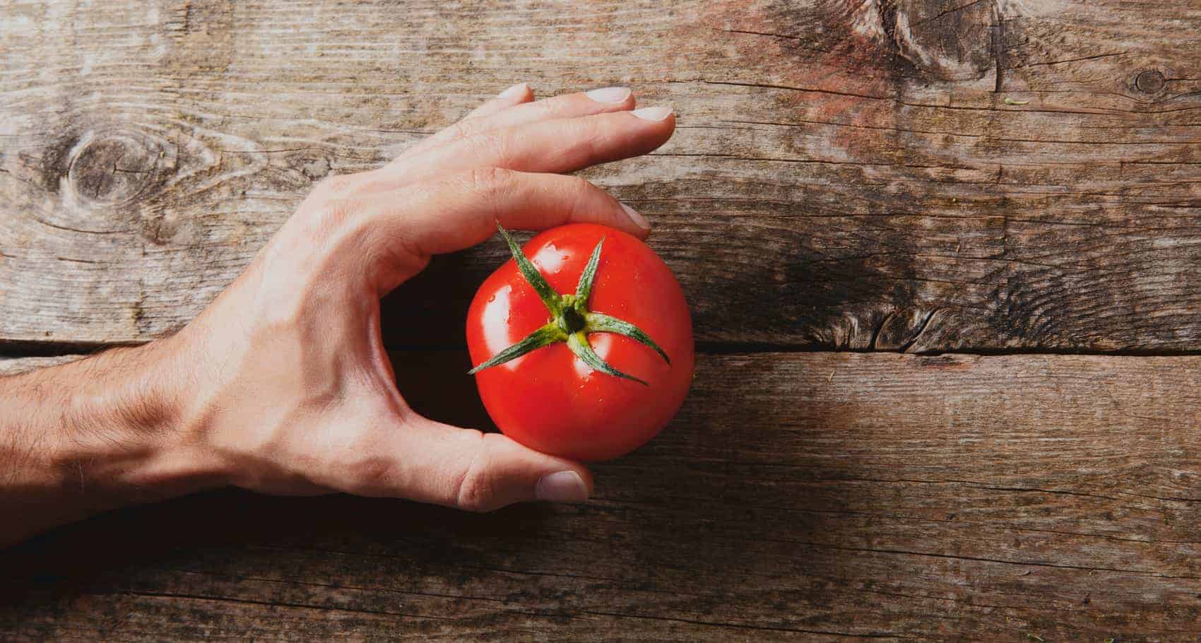 Mano con pomodoro su legno