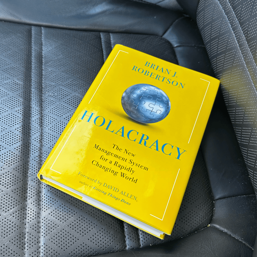 A copy of the book Holacracy by Brian J. Robertson resting on a car seat—picked up from Facebook Marketplace, sparking a deeper reflection on the system’s current relevance and how it pairs with modern productivity frameworks like TimeCrafting.