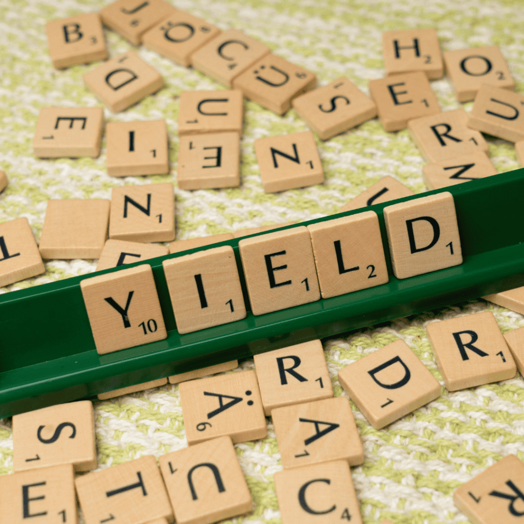 Scrabble pieces strewn about a table with the tiles for YIELD spelled out on the ledge for the player to play next.