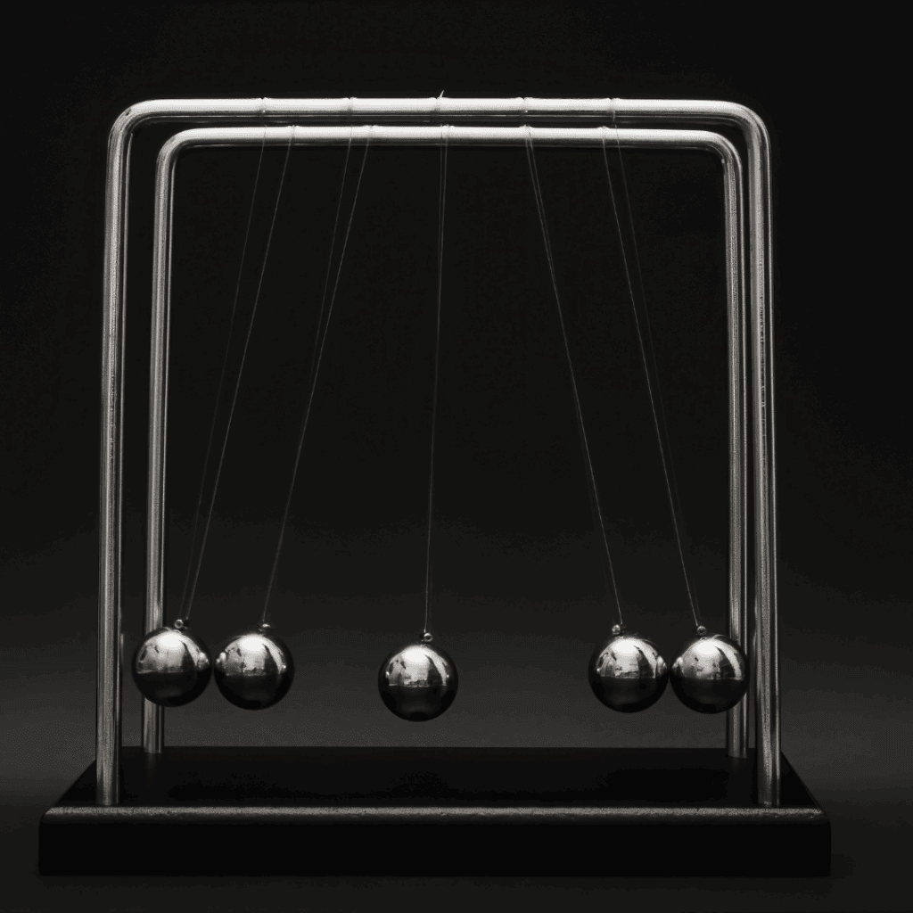 A Newton’s cradle with five suspended metal balls, symbolizing the transfer and rhythm of momentum against a dark background.