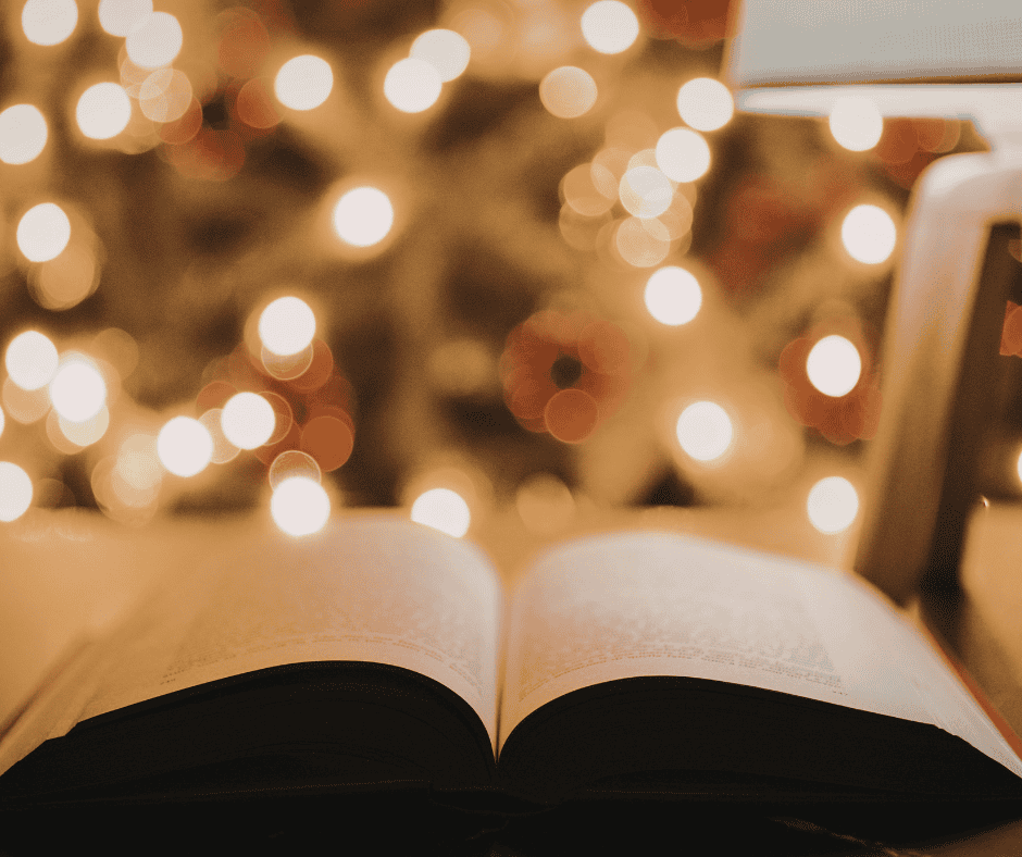 A serene scene featuring an open hardcover book face up on a table in front of blurry holiday lights.