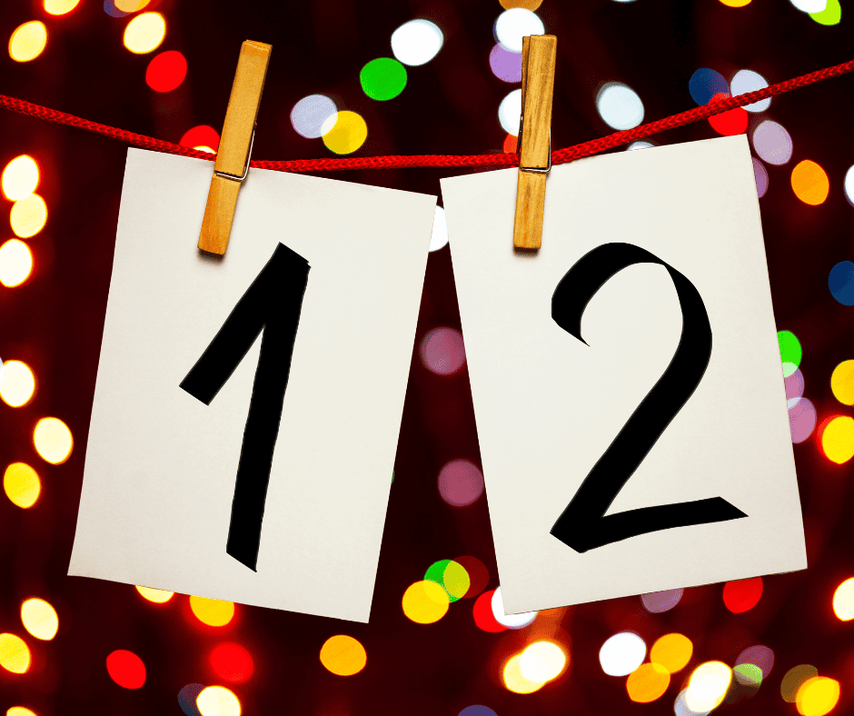 The numbers 1 and 2 written on white cards hanging by clothespins on a line with some festive lights blurred behind them.
