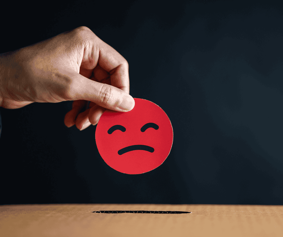 A hand lowering a red sad-face token toward a narrow slot, symbolizing a bad day being dropped or let go.
