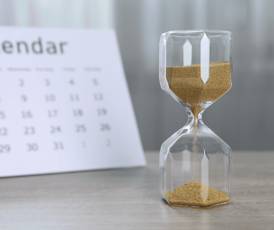An hourglass with golden sand beside a calendar, symbolizing how time passes steadily while the calendar quietly shapes how we engage with our days.