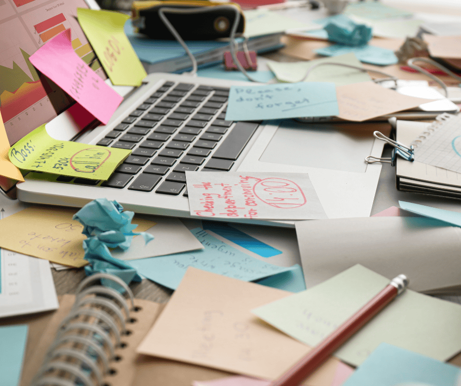 A cluttered laptop workspace covered in colorful sticky notes, loose papers, and reminders, symbolizing overwhelm and cognitive overload.