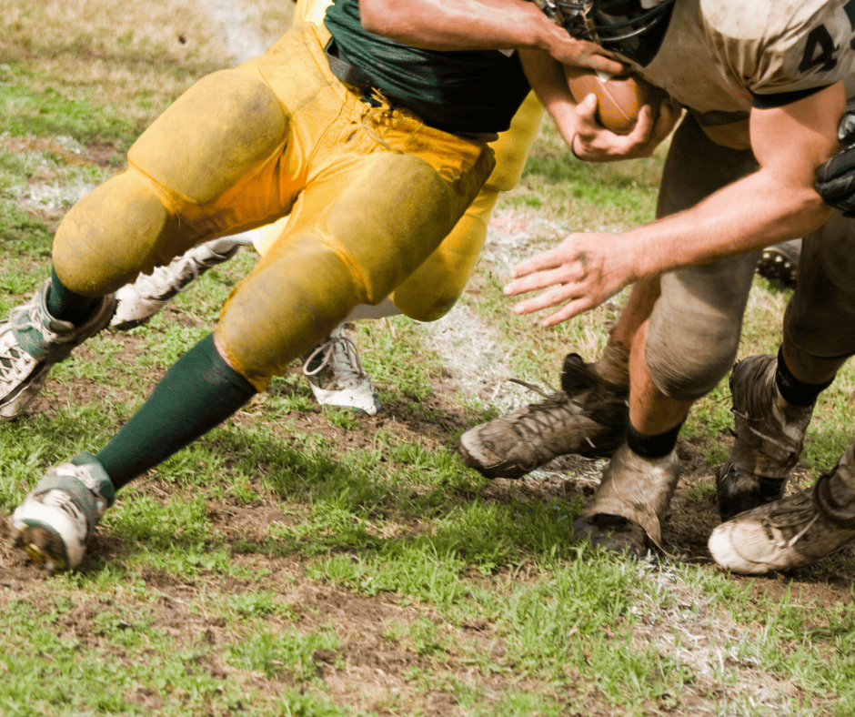 Football player driving forward through a tackle, leaning into contact to gain extra yards with a second effort.