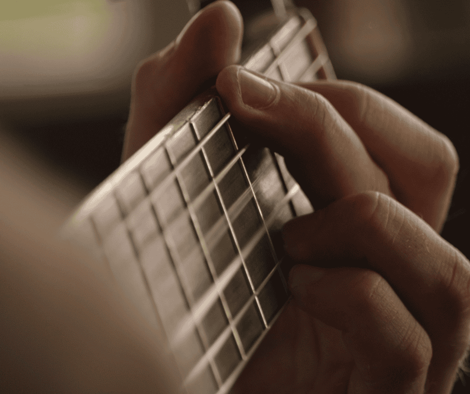Close-up of fingers pressing guitar strings on a fretboard, symbolizing the repetition and discipline required for practice and mastery.